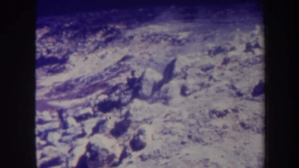 1967 Honolulu 8mm frame of barren rocky terrain, scattered stones, and a low veil of smoke or haze under a strong purple-blue cast.