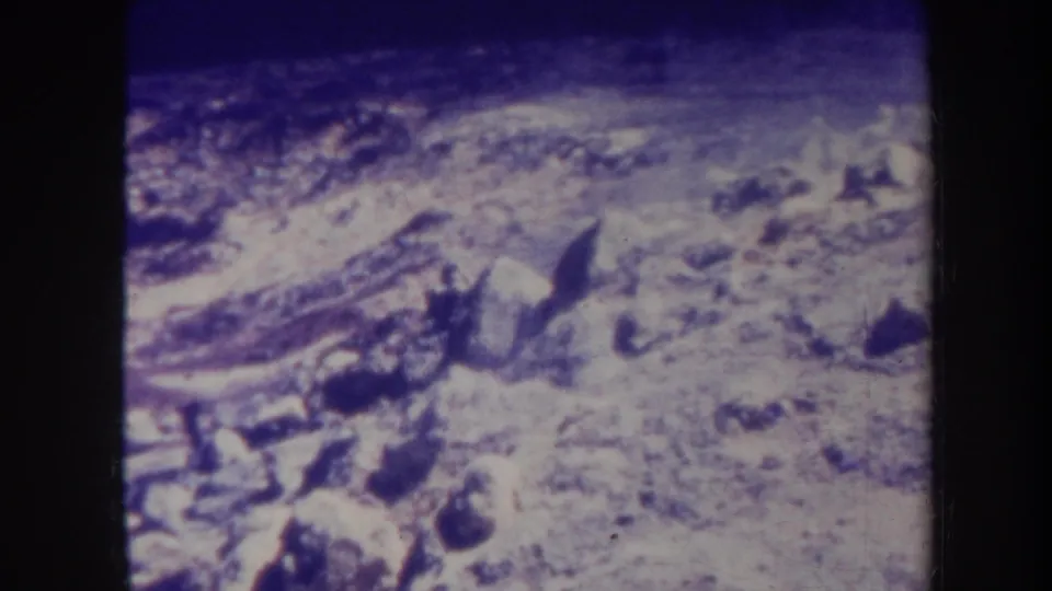 1967 Honolulu home-movie frame holding on rough rocky ground, darker foreground stones, and faint smoke or haze near the top of the view.