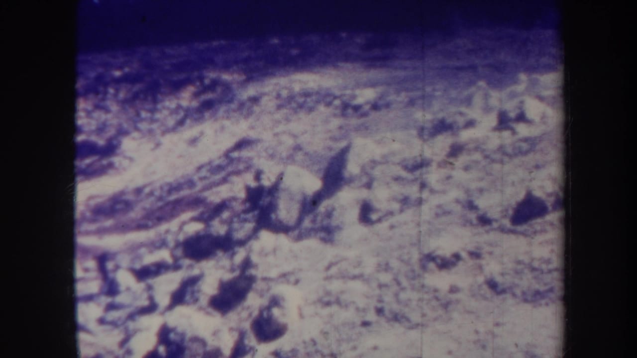 Similar pale hillside view with rocks, rough texture, and dark film borders at the sides.