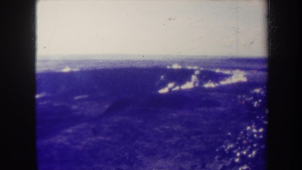 Blue-toned aerial view of mountains or ridges under a pale sky with clouds near the horizon.