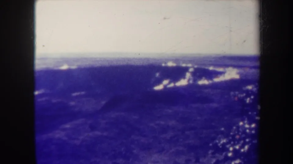 1967 Honolulu-area home-movie frame appears to show an aerial view of blue mountain ridges beneath a pale sky and distant clouds.