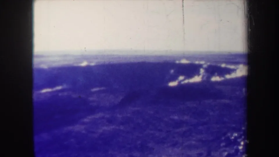 1967 Hawaii home-movie frame showing a soft aerial landscape with dark blue terrain, distant cloud forms, and pronounced aged-film marks.