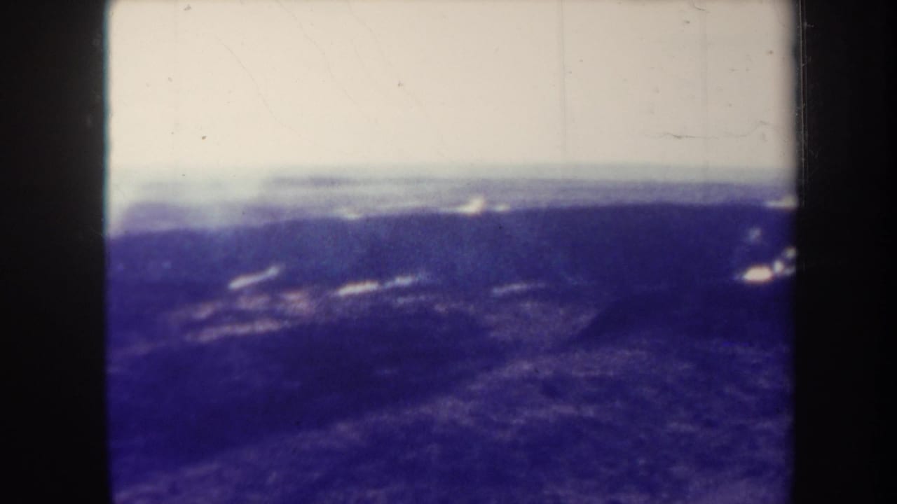 1967 Hawaii 8mm frame showing distant smoke over dark volcanic terrain beneath a pale horizon.