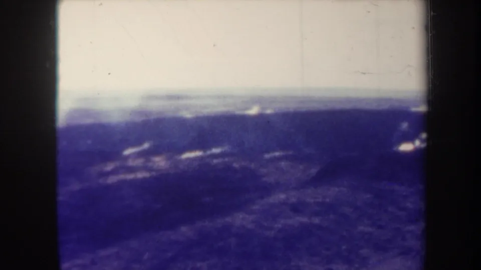 1967 Hawaii 8mm frame showing distant smoke over dark volcanic terrain beneath a pale horizon.