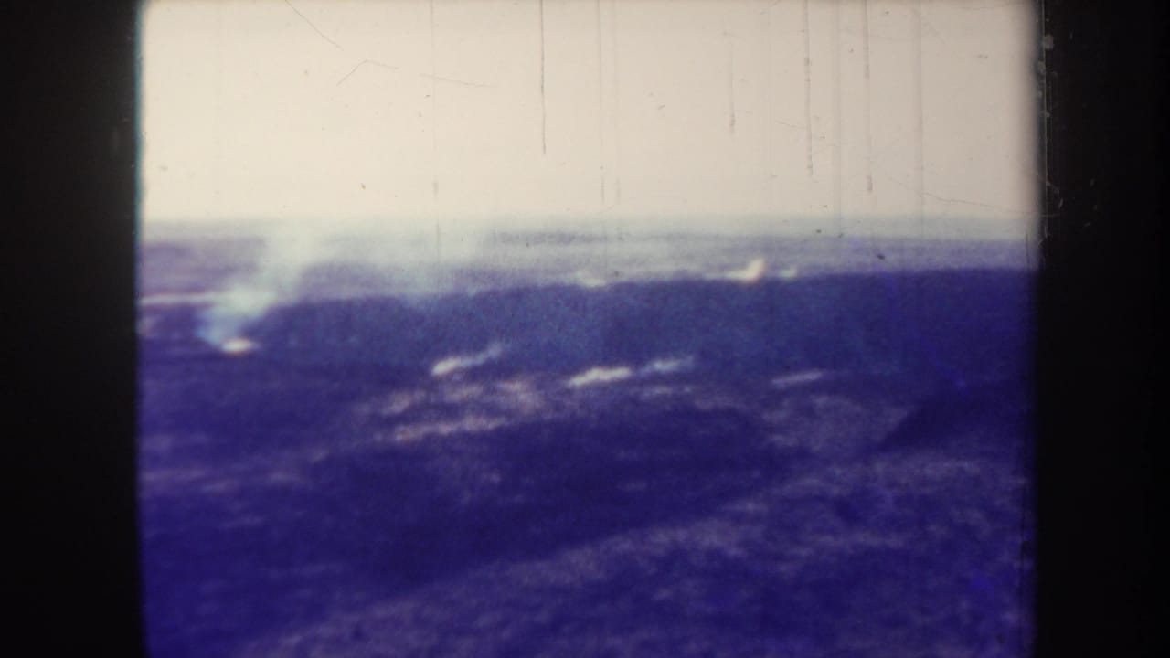 Distant smoke above dark volcanic landscape with visible film borders and scratches.