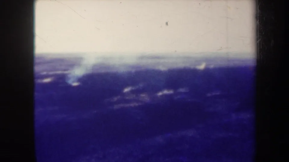 1967 Hawaii 8mm frame with a low smoke plume over dark volcanic terrain and a washed pale sky.