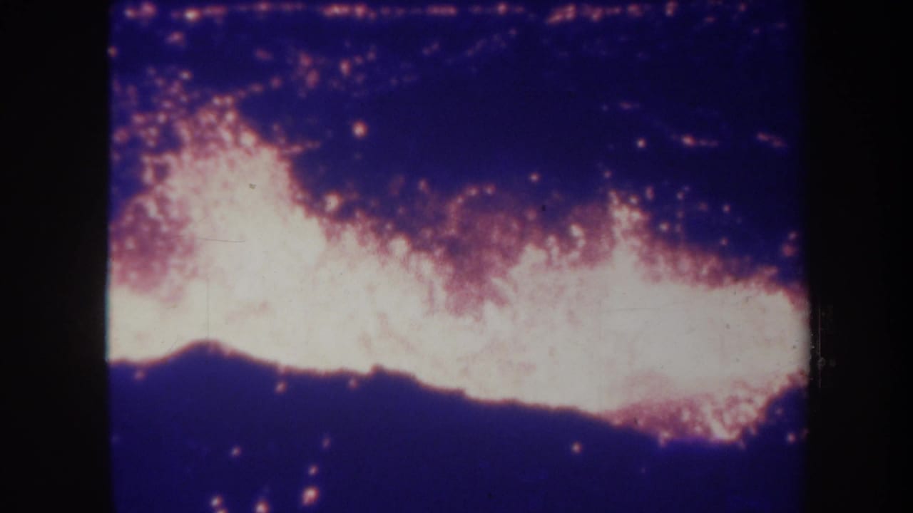 1967 Hawaii 8mm frame showing white-hot lava glow against dark volcanic ground and a blue-purple night sky.