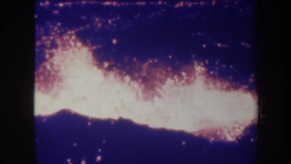 1967 Hawaii 8mm frame showing white-hot lava glow against dark volcanic ground and a blue-purple night sky.