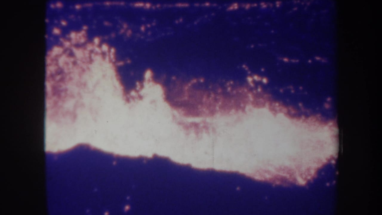 Lava flare brightens across the center of a dark nighttime volcanic view.