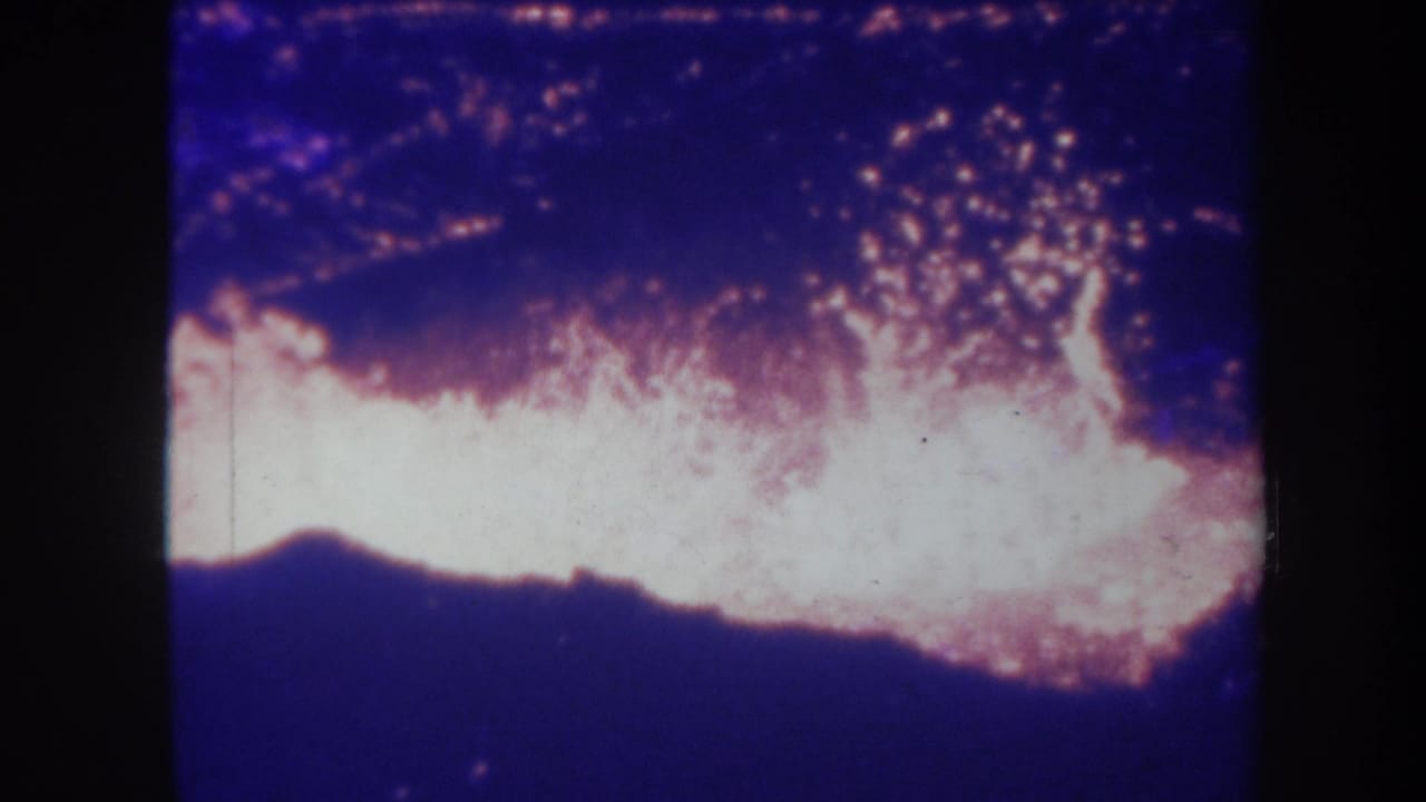 1967 Hawaii 8mm frame showing bright volcanic glow or lava-like activity under a dark sky, with grain and color fading.