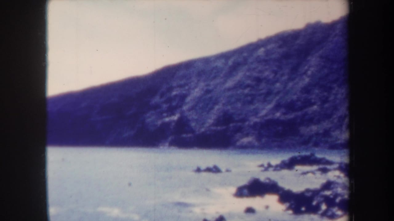 Coastal rocks in calm water beneath a large sloping cliff.