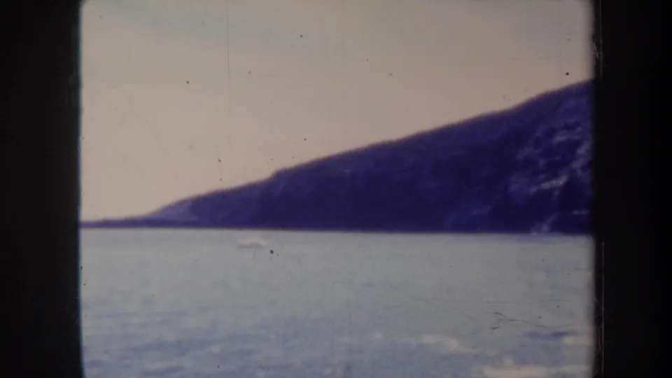 Final 1967 Honolulu coastal frame showing calm water below a shadowed cliff, with aged 8mm color and visible film wear.