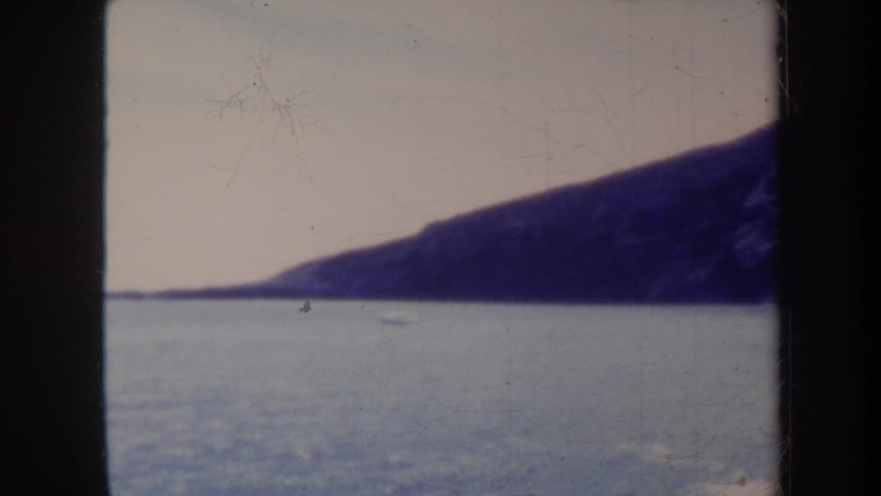 Calm blue water below a pale sky with a dark sloping landmass in the distance.