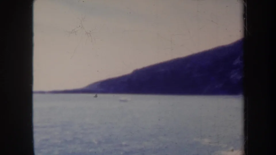 1967 Honolulu-area 8mm frame showing calm blue water, a pale sky, and a dark distant coastal landmass through black film borders.