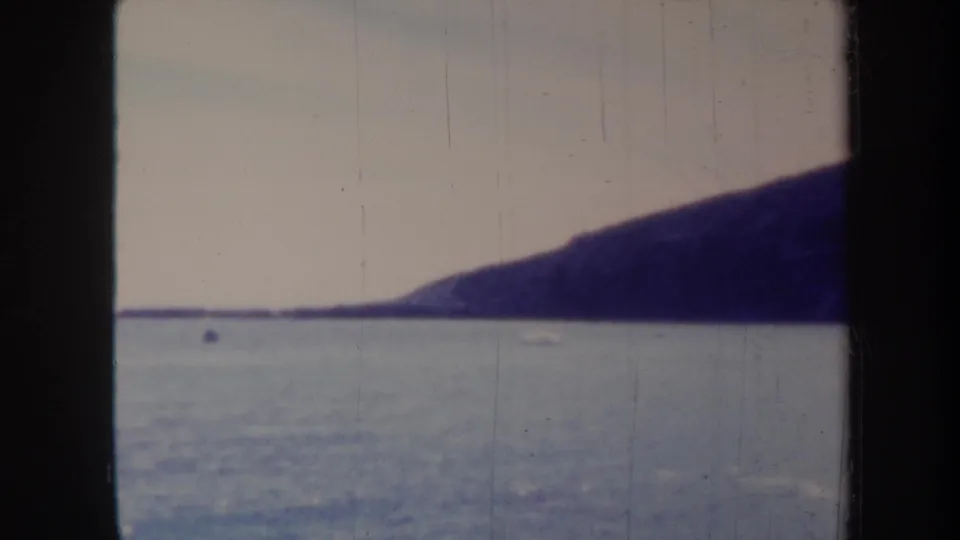 1967 Honolulu-area coastal view with a dark headland, quiet blue water, pale sky, and visible 8mm scan borders.