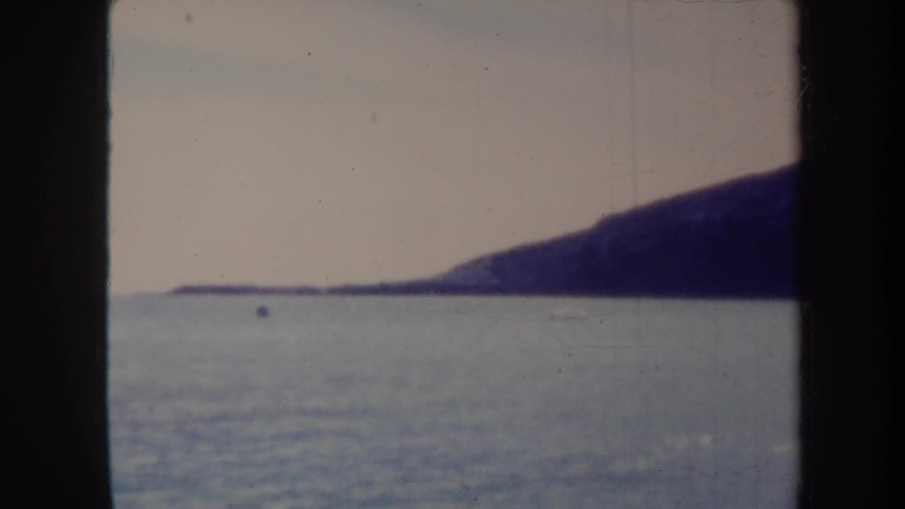 1967 Honolulu-area 8mm frame showing ocean water, a distant dark hillside, and heavy film gate borders before the church view appears.