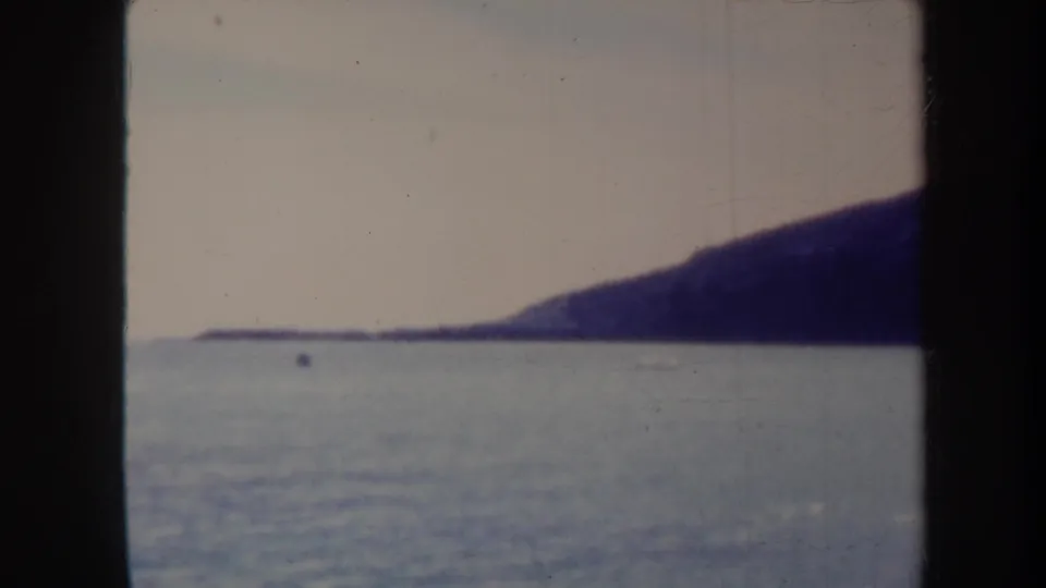 1967 Honolulu-area 8mm frame showing ocean water, a distant dark hillside, and heavy film gate borders before the church view appears.