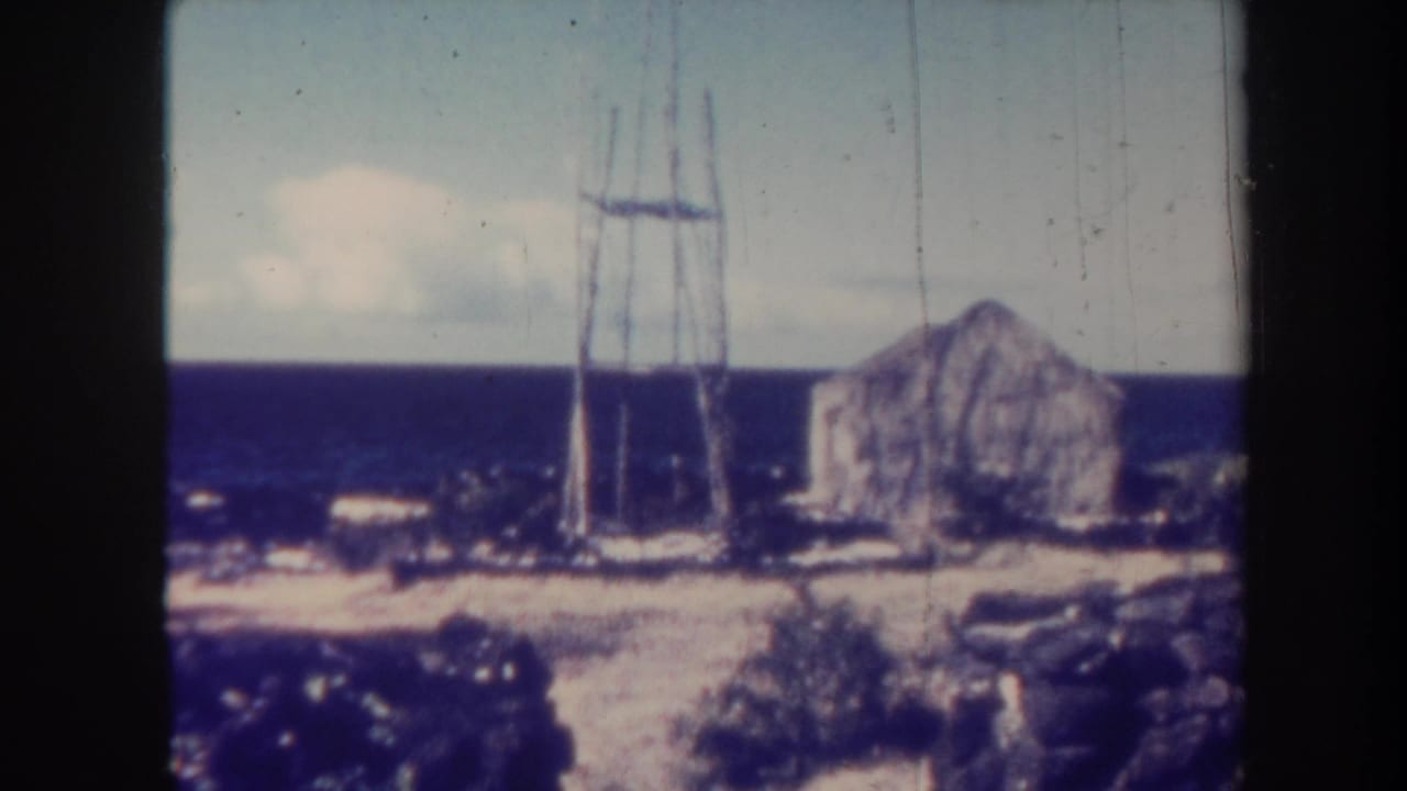 Coastal hillside with a metal tower, stone building, ocean horizon, and clouds.