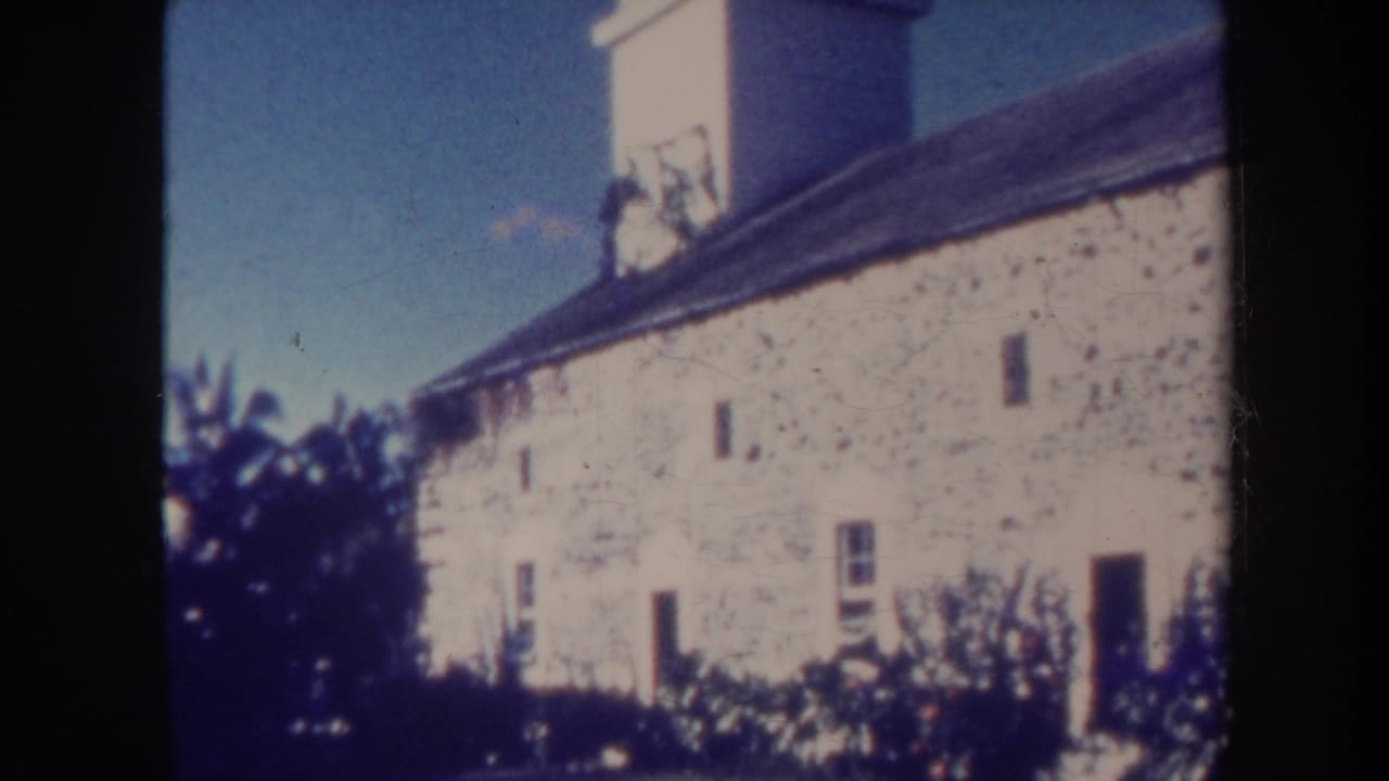 Stone building facade with white tower edge, doorway, windows, roofline, and trees.