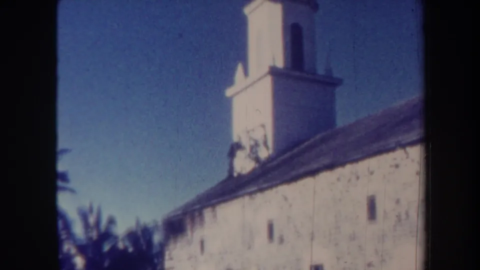 1967 Honolulu 8mm frame showing the white bell tower above the stone building, with blue sky and foliage at the edges.
