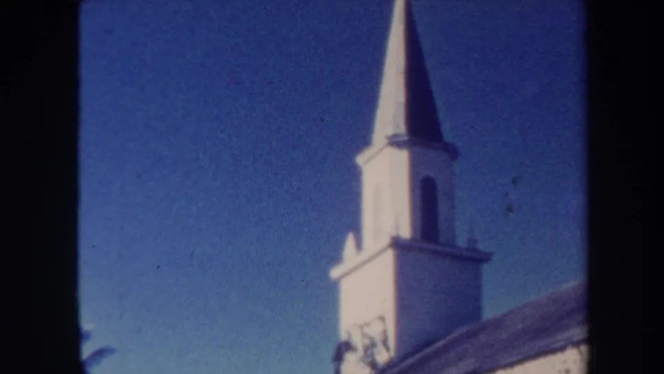 1967 Honolulu frame focused on the white steeple and bell tower above the dark roof, with clear blue sky behind it.
