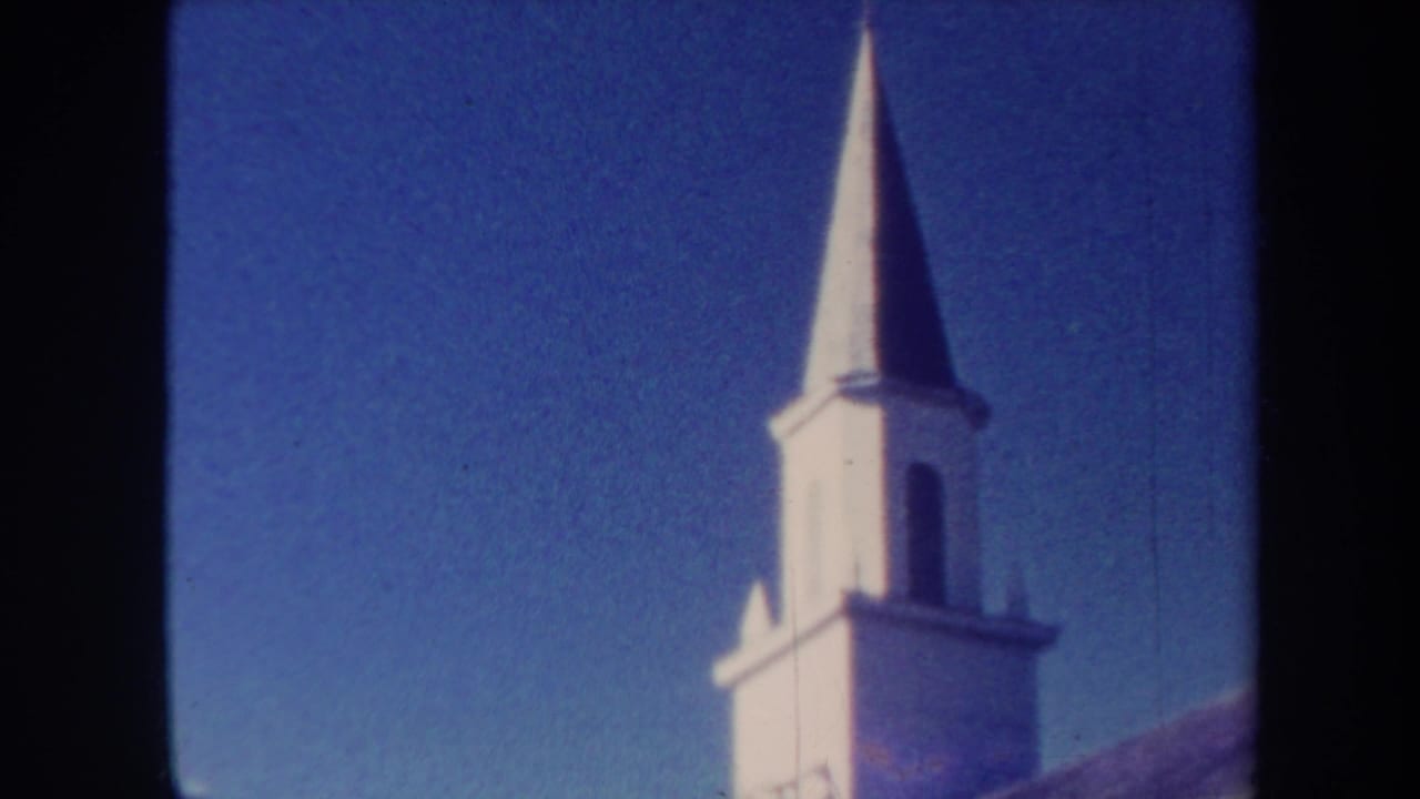 White church-like steeple against a deep blue sky, framed by dark film borders.