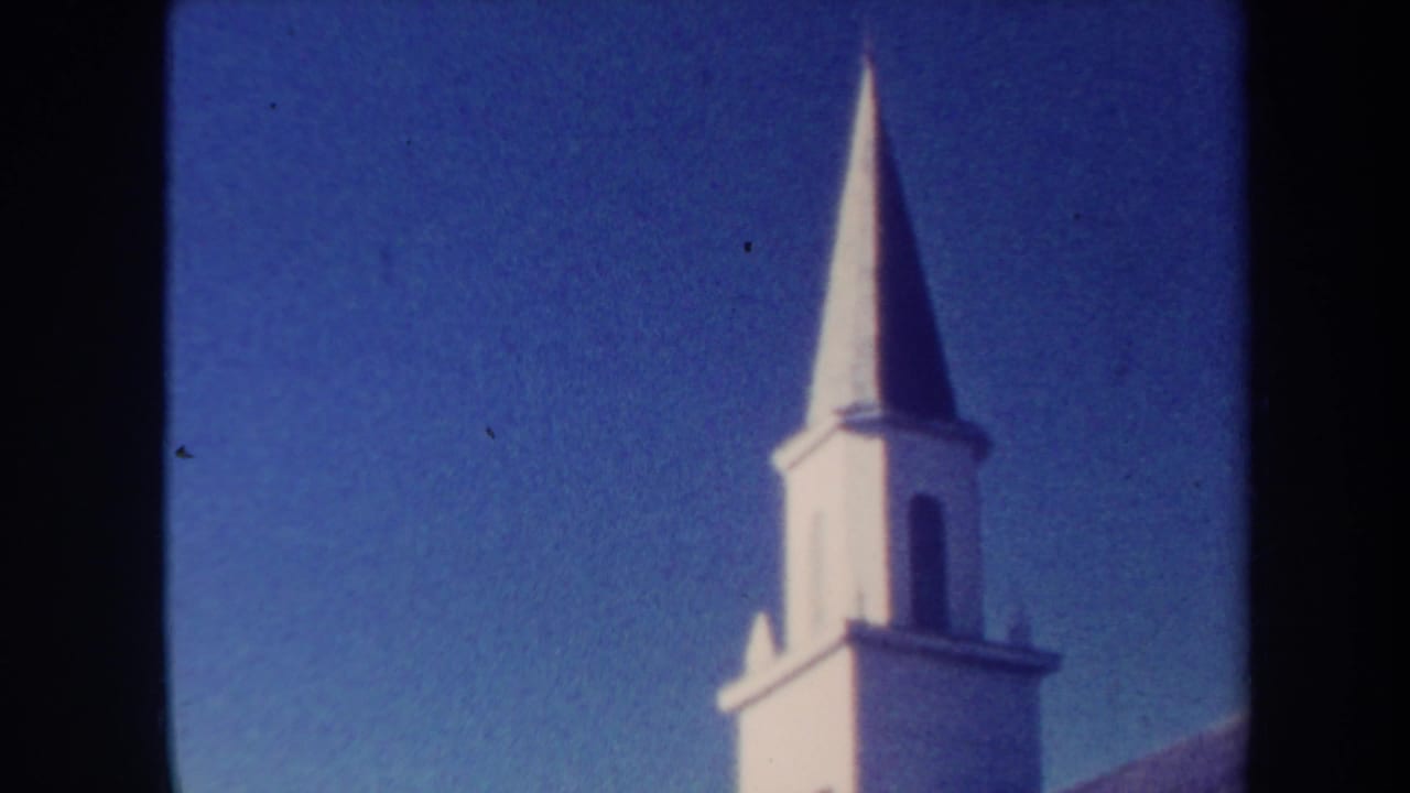 White steeple and partial roofline under a deep blue sky with film grain.