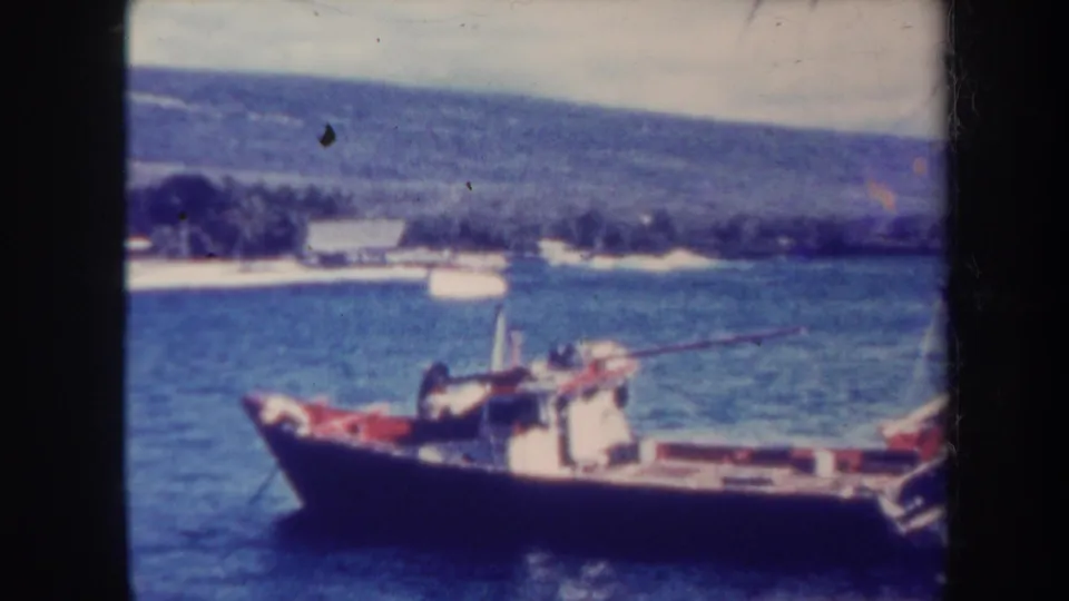 1967 Honolulu frame of a small fishing boat near a tropical shoreline, backed by hazy hills and soft 8mm color.