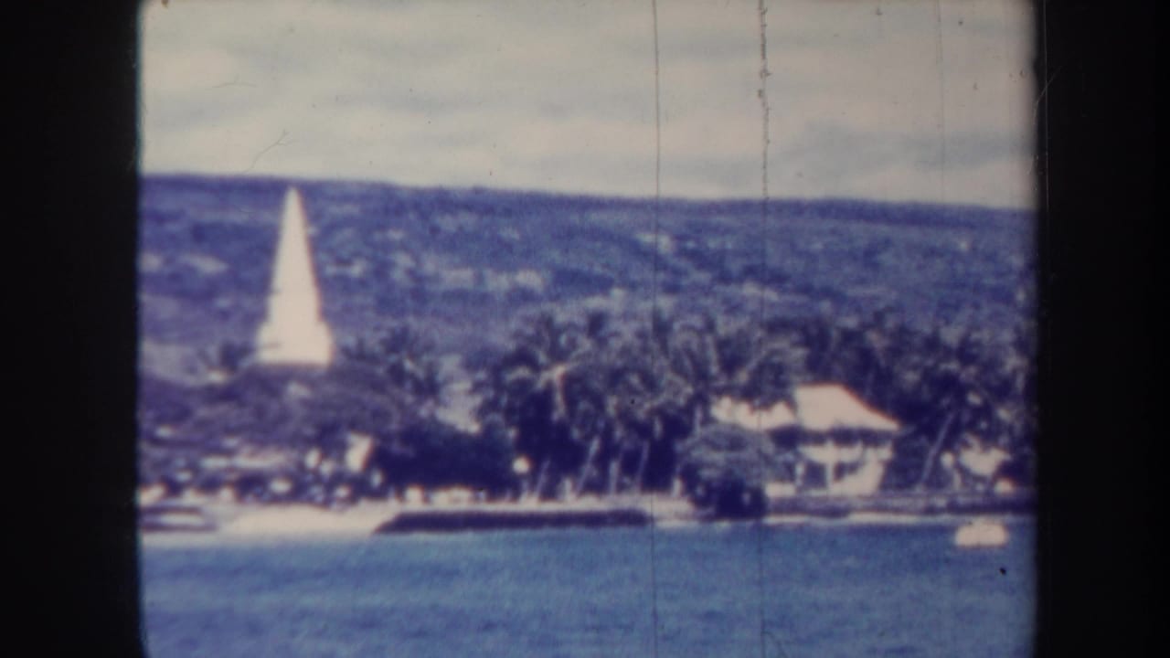 Coastal water, palm trees, shorefront buildings, and a white obelisk on a distant hillside.