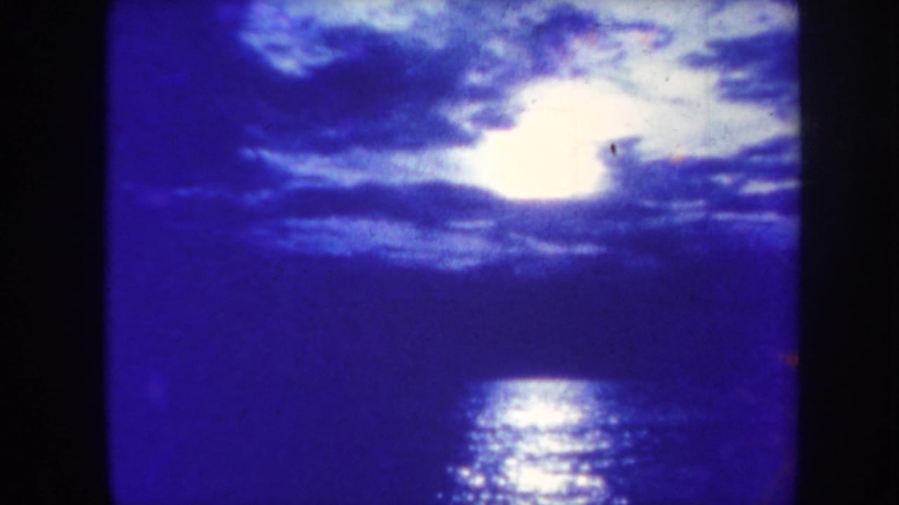 Bright moon behind clouds reflecting on dark ocean water.