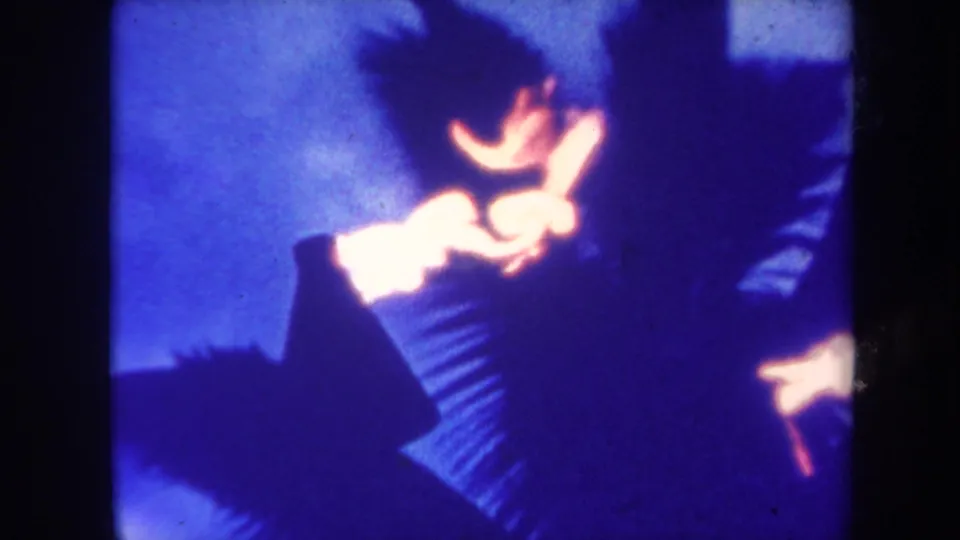 Honolulu 1967 home-movie frame showing a dark figure, bright torch fire, and palm fronds in blue night exposure.