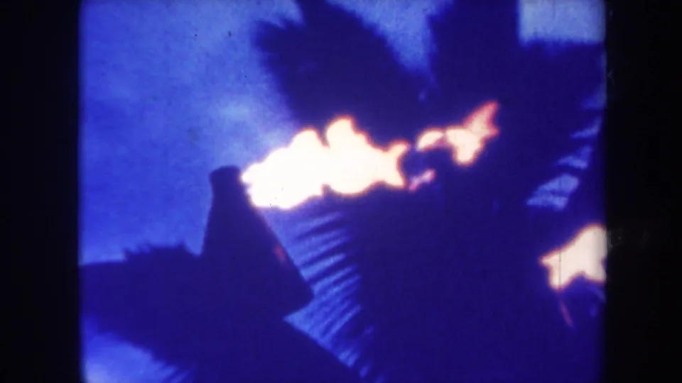 1967 Honolulu 8mm frame with firelight crossing a silhouetted figure against palm fronds and a blue night background.