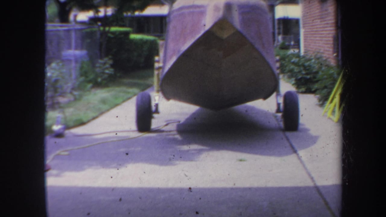 Boat bow on a wheeled trailer parked in a suburban driveway.