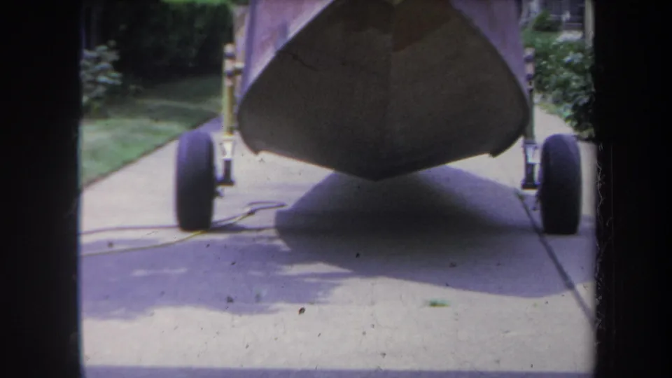 A low, closer 8mm frame centers the boat bow above the trailer axle and wheels on a suburban driveway.