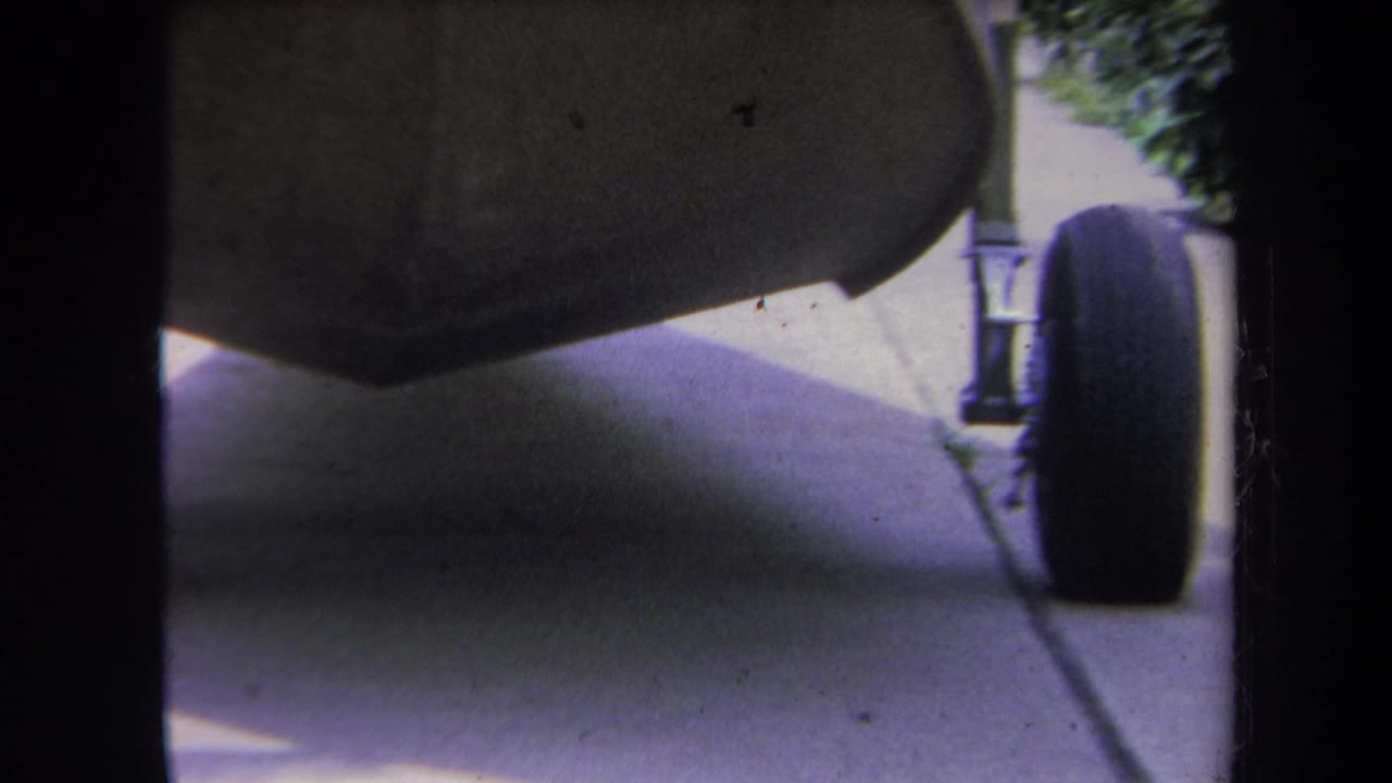 1969 Yucaipa home-movie frame showing a dark stroller wheel, underside, shadow, and sidewalk from ground level.