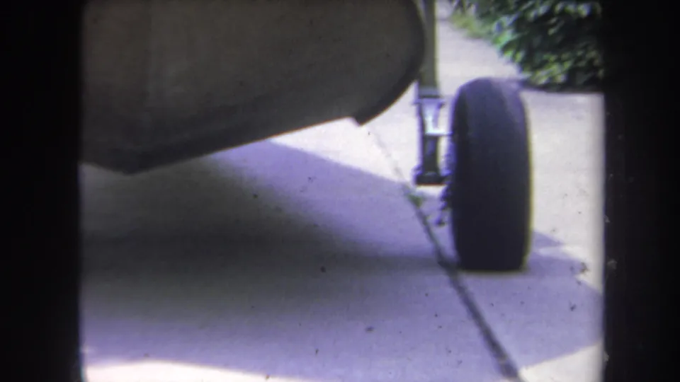 Ground-level 1969 Yucaipa frame with a stroller wheel, metal support, sidewalk seam, hedge, and 8mm frame border.