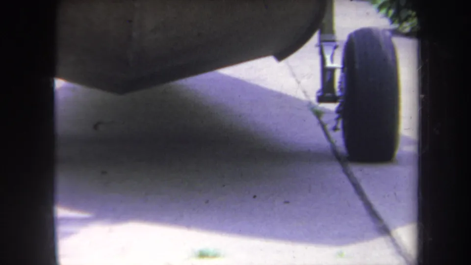 1969 Yucaipa 8mm frame showing the stroller underside and tire close to camera over a shaded concrete sidewalk.