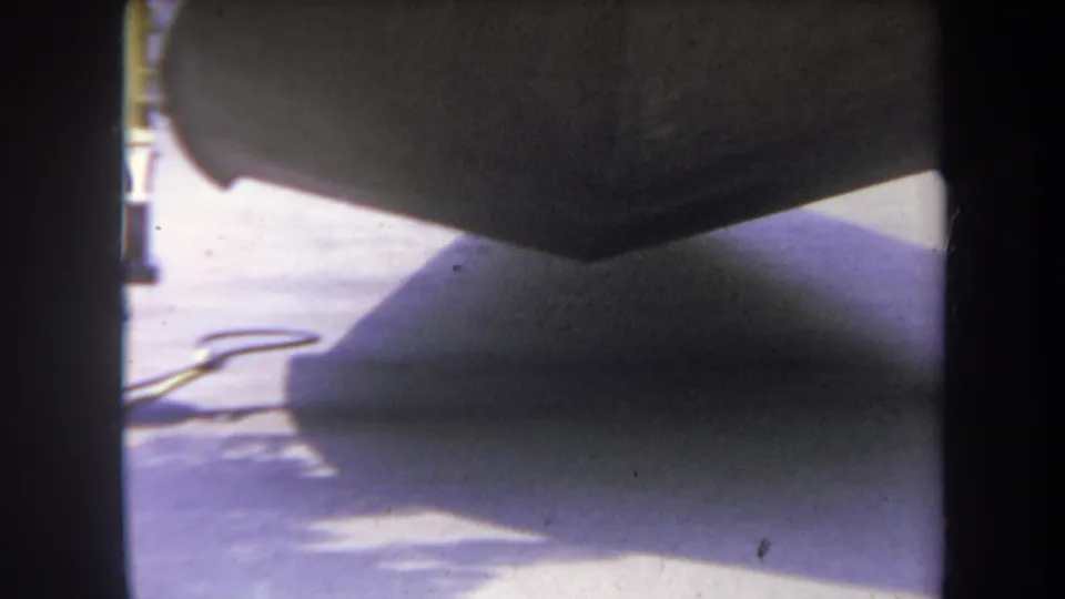 Final 1969 Yucaipa frame with the stroller body overhead, pavement shadow, sidewalk, and a small cord-like object on the ground.