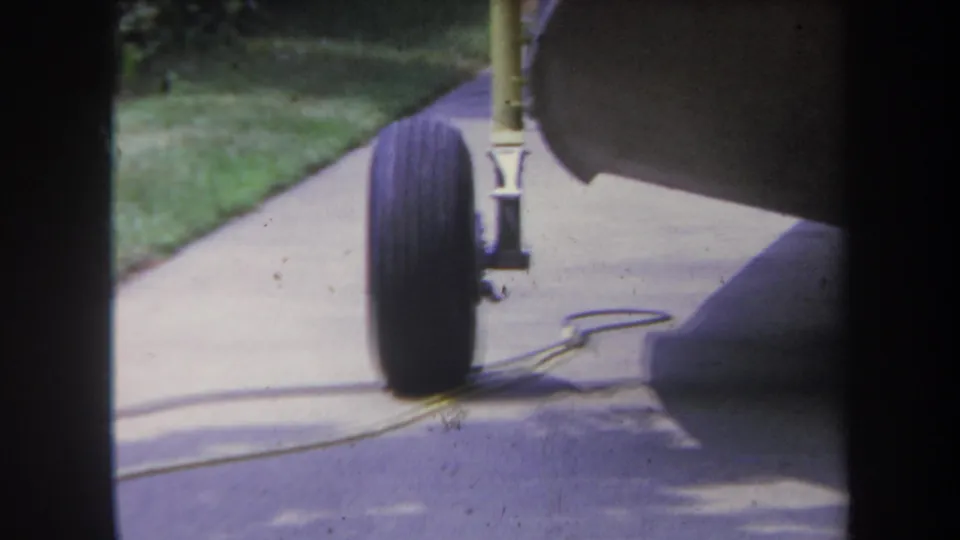 Close 8mm view of a boat or recreational trailer wheel on a Yucaipa driveway, with lawn, cord, and shaded trailer underside.