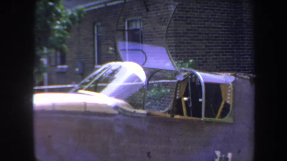 Final 1969 Yucaipa frame showing the parked aircraft's canopy, wing, and open cockpit against a residential brick exterior.