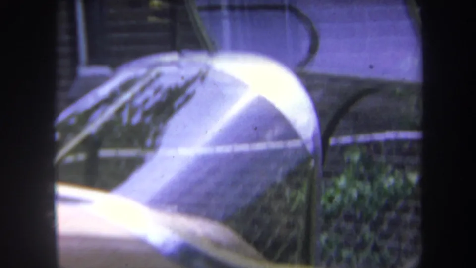Close 1969 8mm view of the gold-colored car's rounded hood and windshield, softened by reflections and film fading.