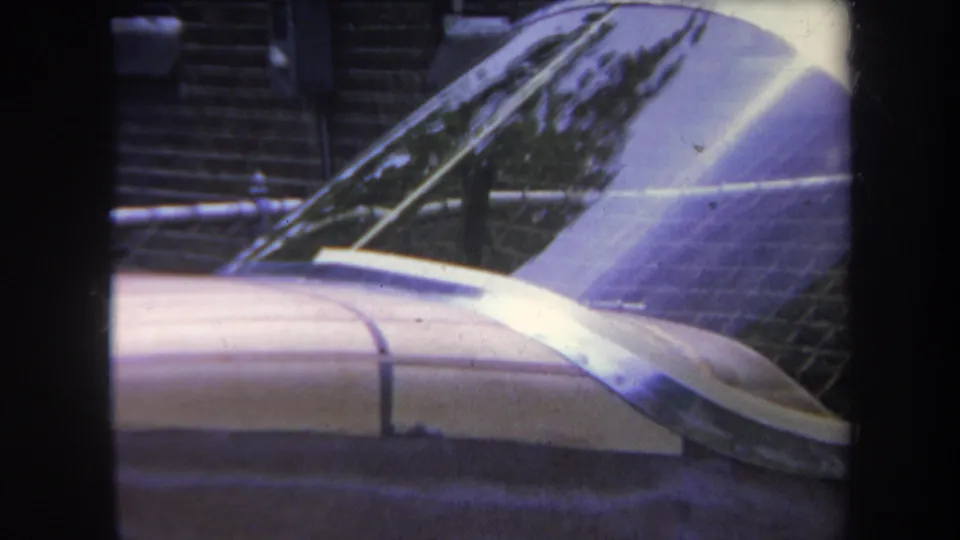 1969 Yucaipa-area 8mm frame showing the car windshield and hood beside a brick building, with reflective streaks across the view.