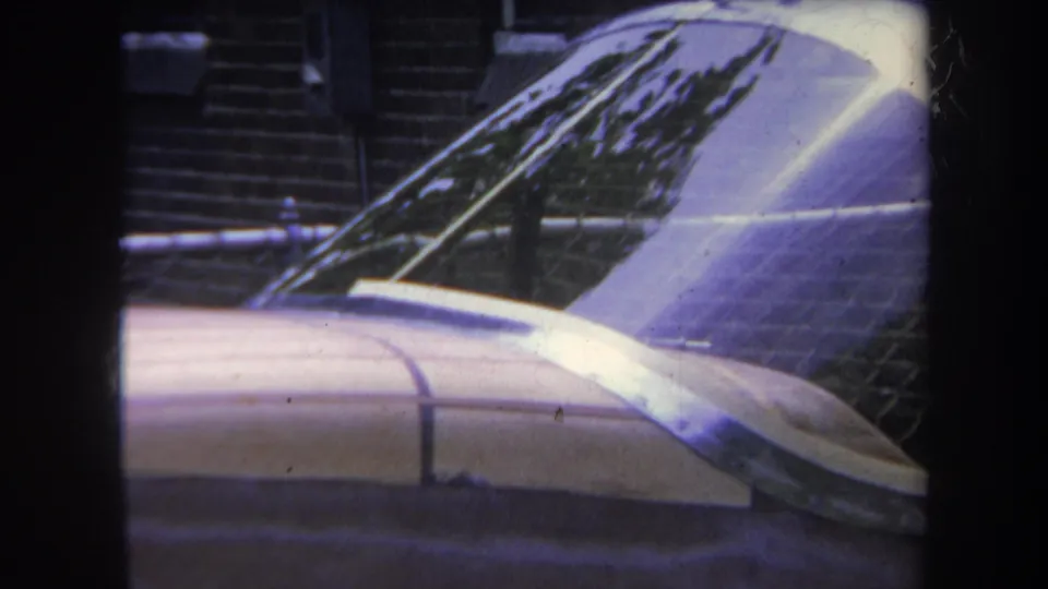 1969 Yucaipa home-movie frame showing a parked small aircraft fuselage and dome-like windshield with brickwork in the background.