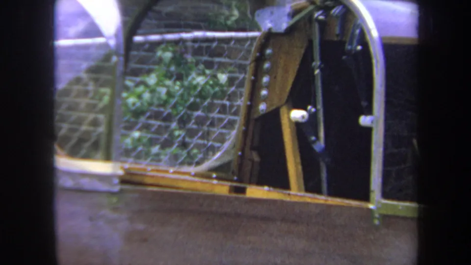 Close 1969 Yucaipa home-movie view of the aircraft cockpit opening, wood trim, dark interior surfaces, and fence behind it.