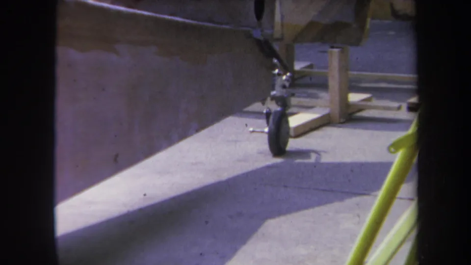 1969 Yucaipa frame focused on the rear landing gear under an unfinished aircraft fuselage with wood support pieces nearby.