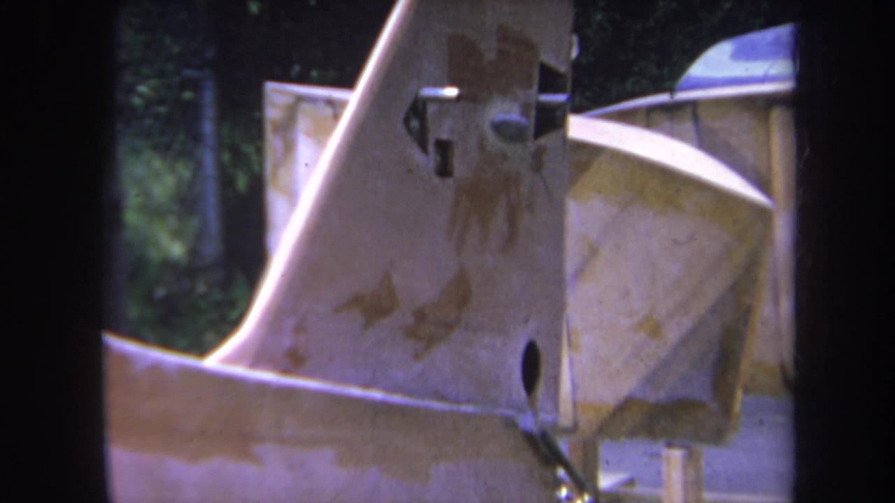 1969 Volmer, Yucaipa 8mm frame showing a close-up of weathered industrial machinery with rust stains, bolts, greenery, and fencing.