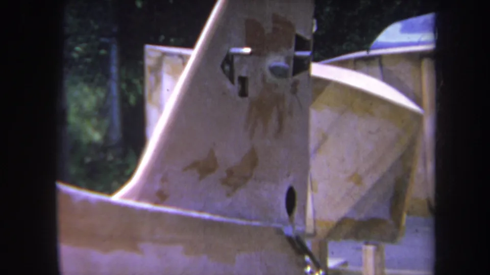1969 Volmer, Yucaipa 8mm frame showing a close-up of weathered industrial machinery with rust stains, bolts, greenery, and fencing.