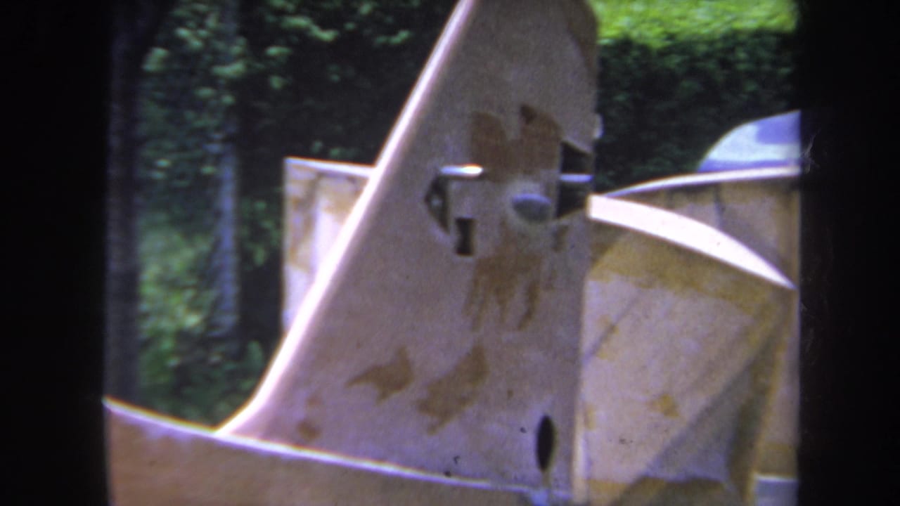 1969 Yucaipa home-movie frame showing a close view of an unfinished model airplane tail area and adjacent green-painted structure.
