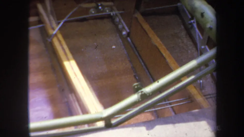 Close 8mm frame of a green-painted model airplane structure crossing exposed wooden ribs and internal rods in 1969 Yucaipa footage.