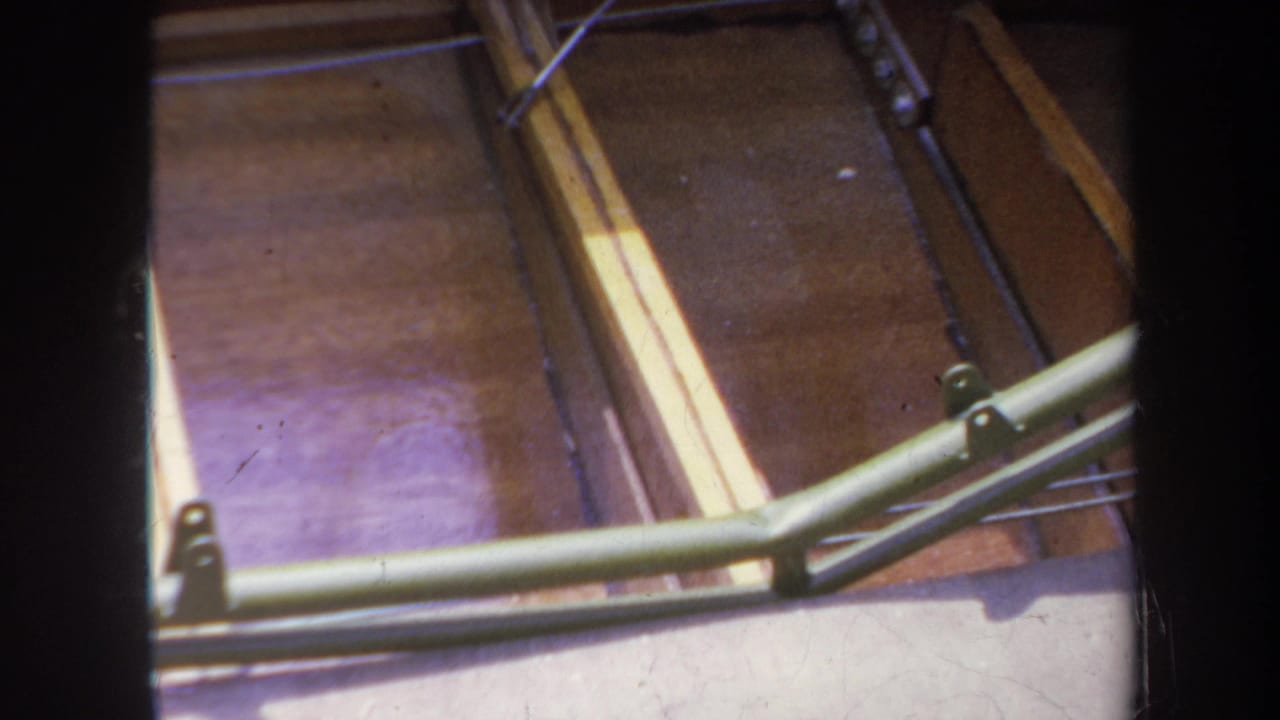 1969 Yucaipa home-movie frame showing wooden boat interior planks, pale strips, and a green metal support brace in sunlight.